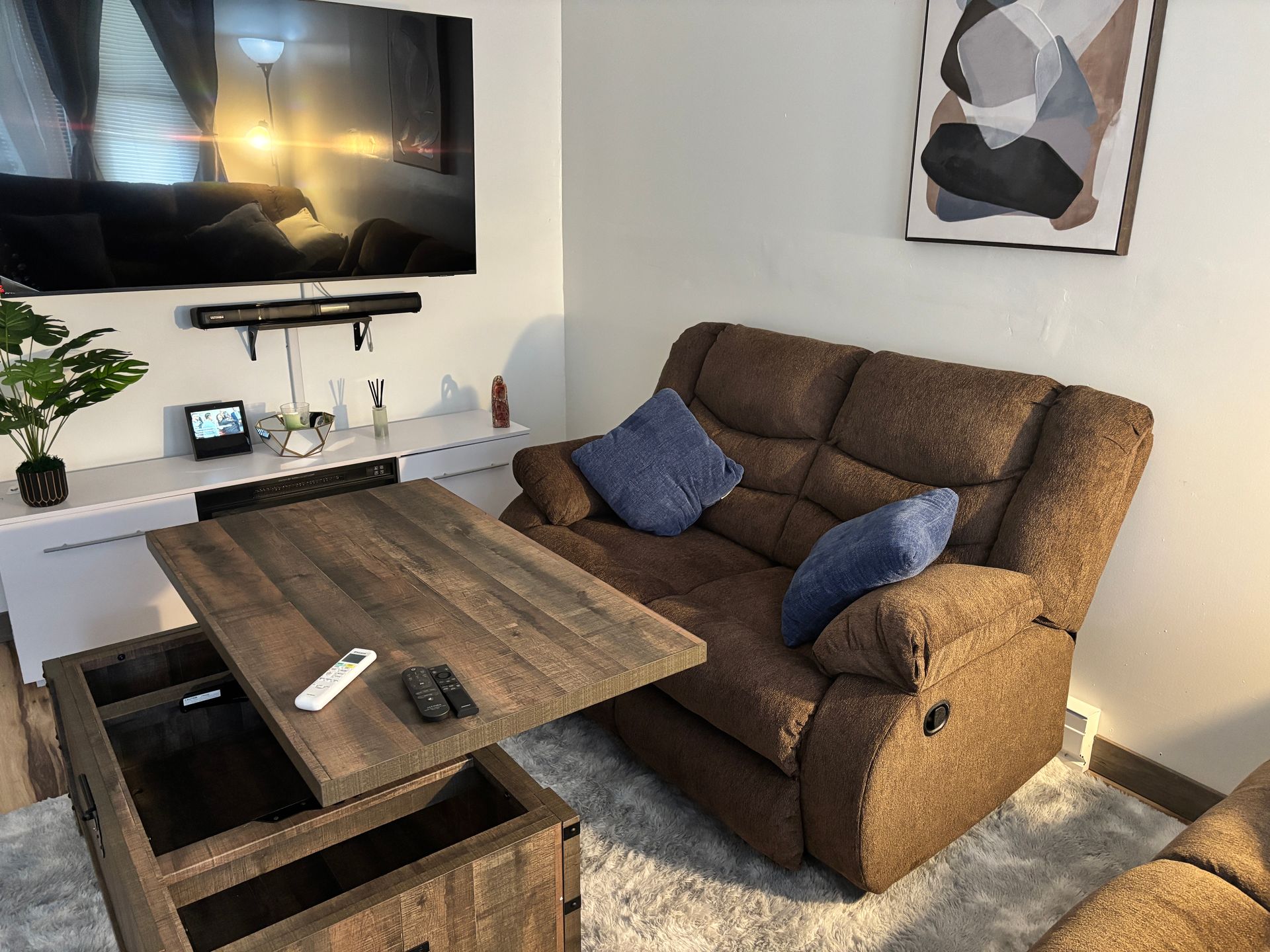 A living room with a brown recliner, lift-top coffee table, TV, and abstract wall art.