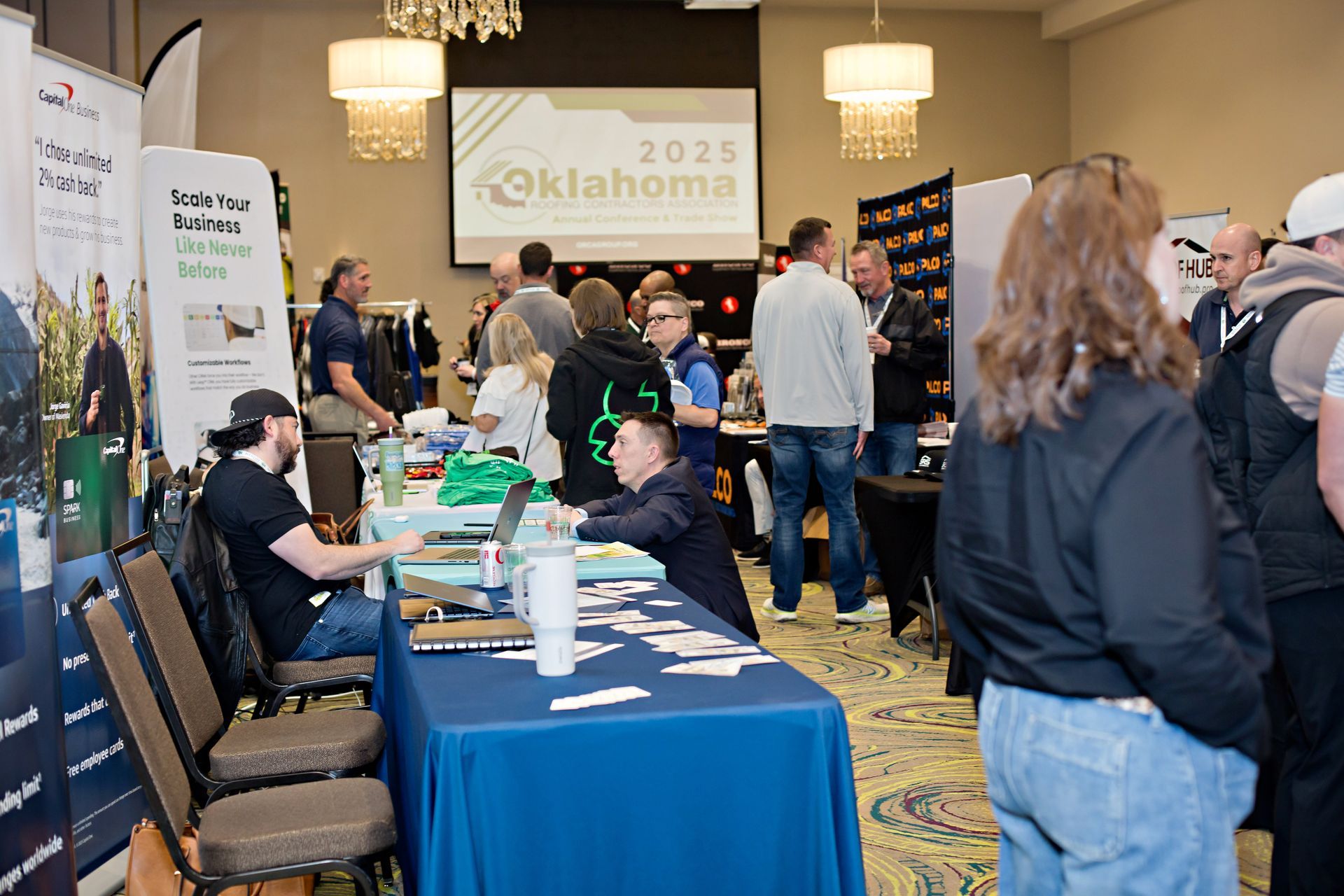People at a conference in a hotel, with display booths and presentations about Oklahoma 2025.