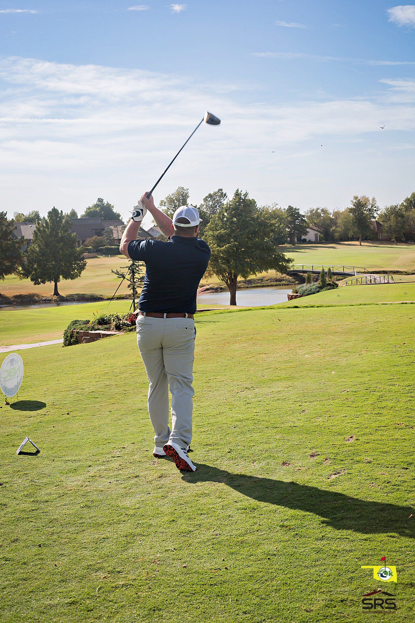 Golfer in a follow-through swing on a sunny golf course, preparing to tee off.