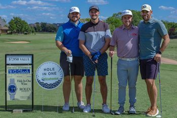 Four men on a golf course pose near a 