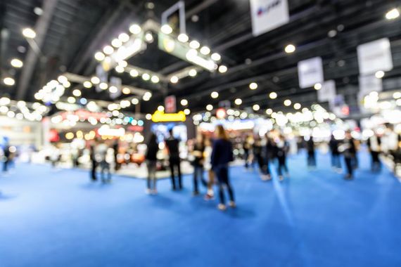 Blurred view of an exhibit hall with a blue floor, people, and vendor booths.