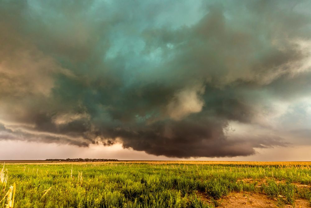 Dark storm clouds gathering over a green field with a distant tree line.