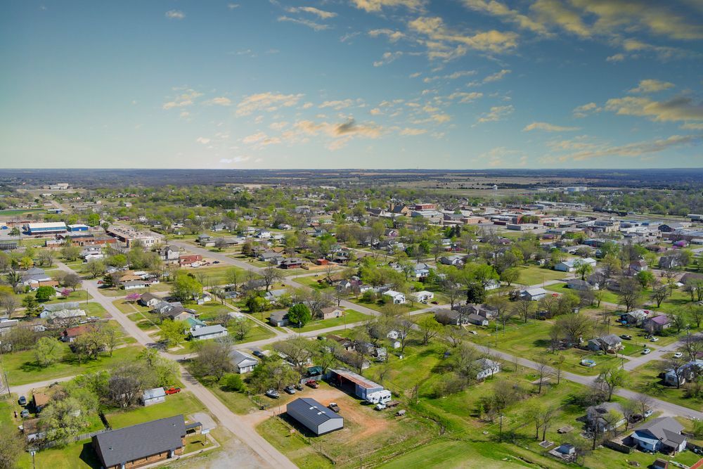 Aerial view of a small town with houses, trees, and buildings under a partly cloudy blue sky.