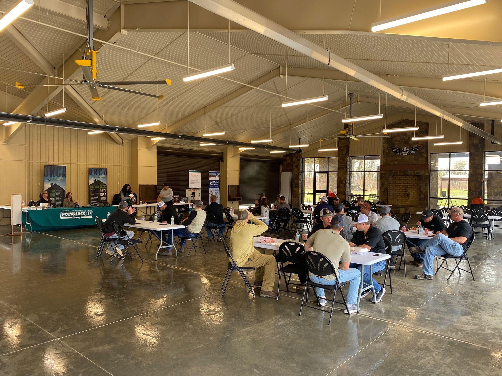 Large indoor space with people sitting at tables, some are interacting with each other.
