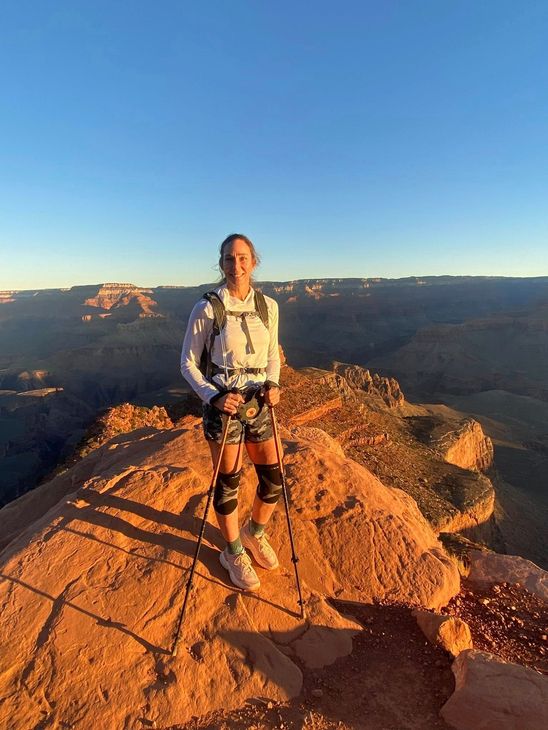 A woman is sitting at a desk with a laptop and a vase of flowers.