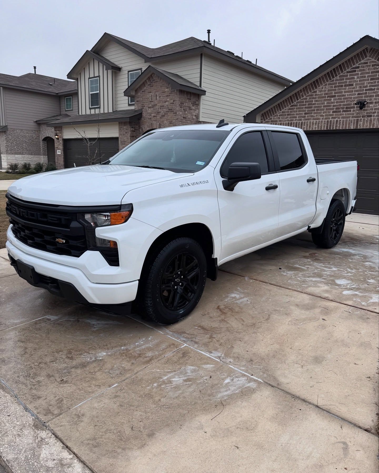 White Chevrolet Silverado truck parked in front of a house. Black wheels, tinted windows. Cloudy day.