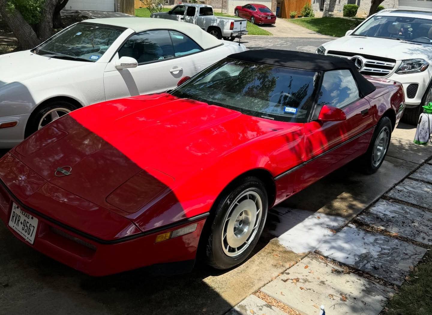 Red convertible Corvette, black top, parked next to a white car, in a driveway.