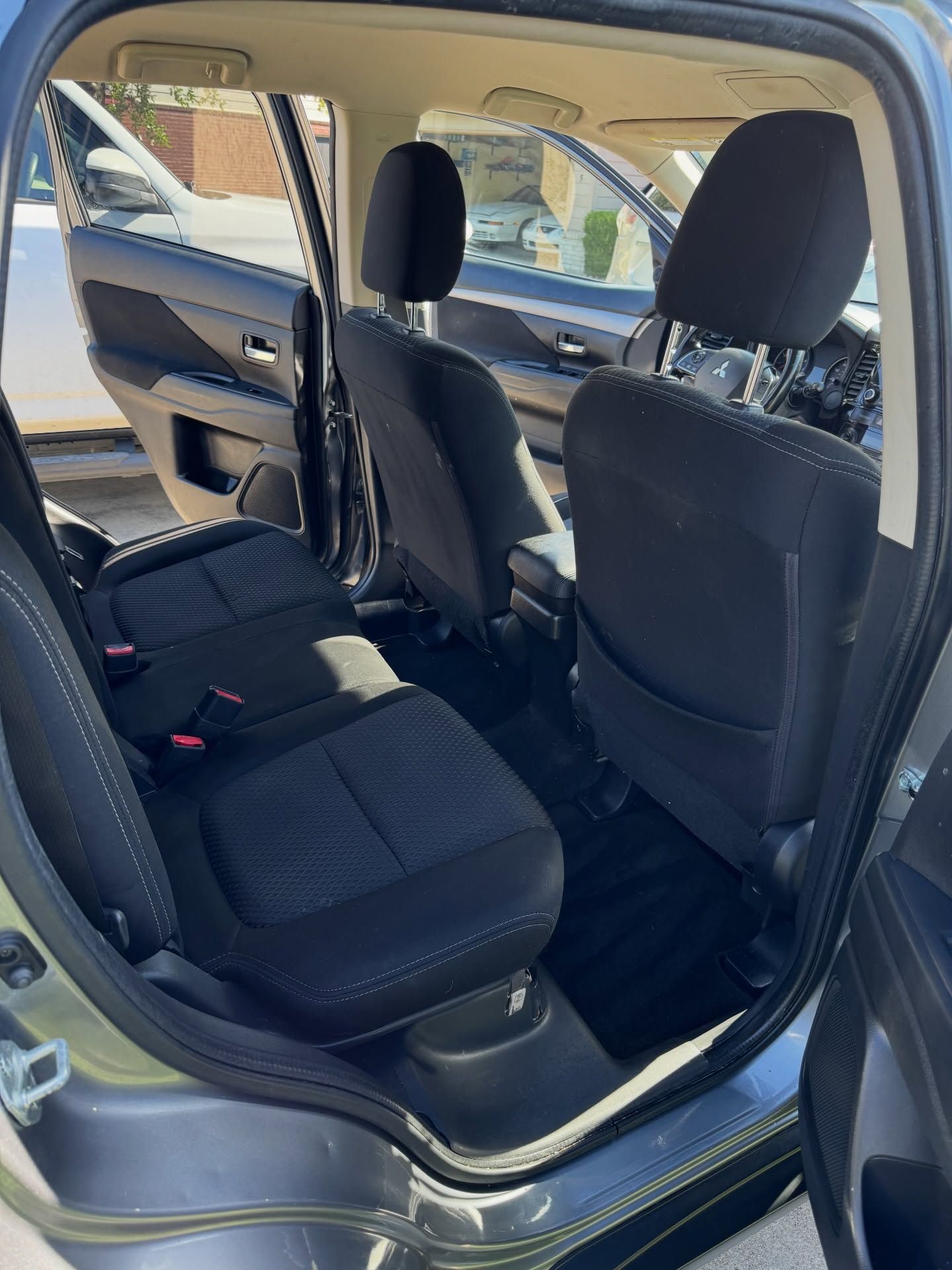Interior view of a gray car's backseat with black seats and dark floor mats. The door is open.