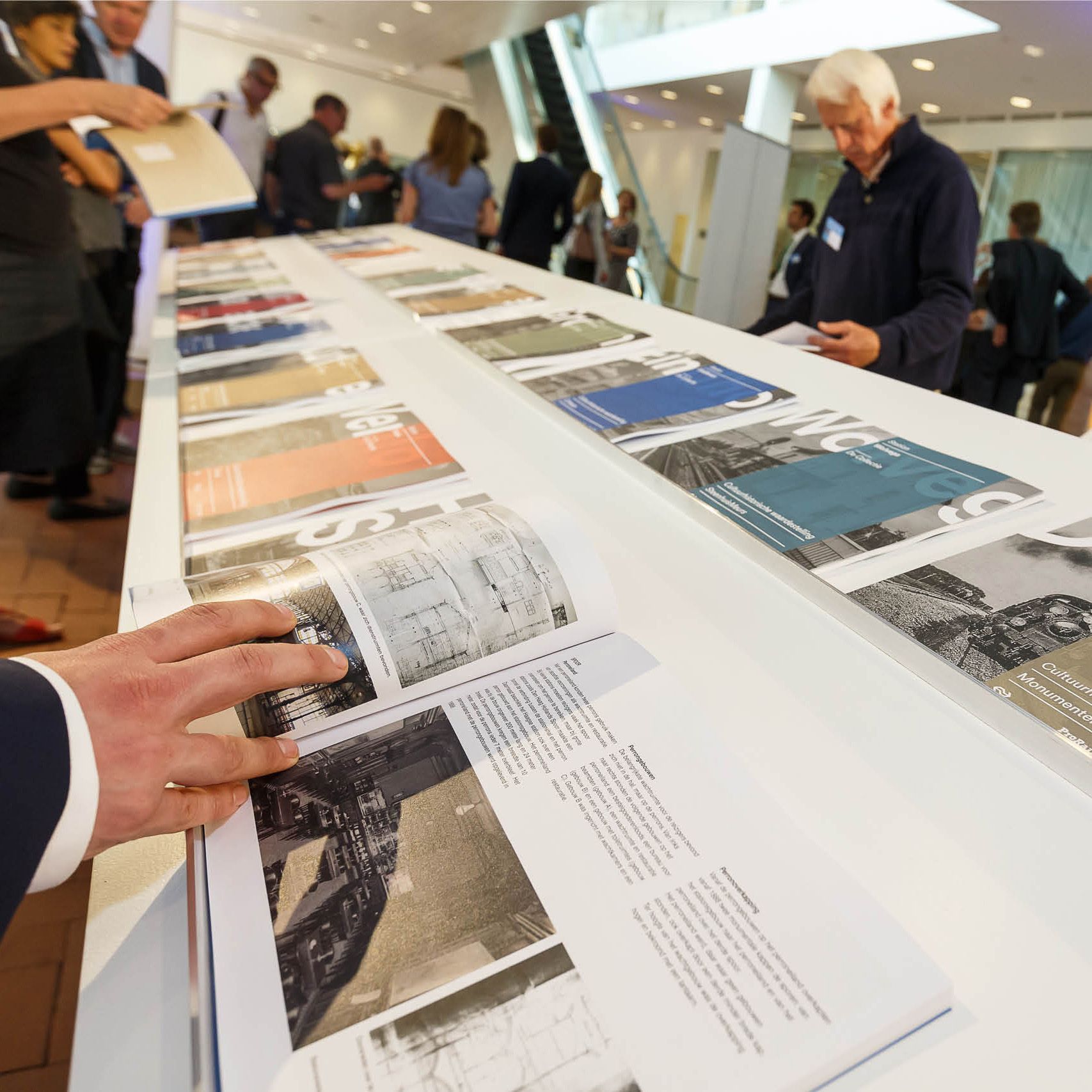 Mensen kijken naar open boeken die op een lange witte tafel binnen liggen.