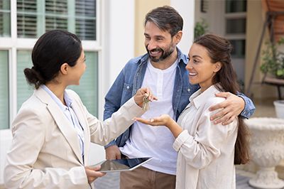 Real estate agent handing keys to a smiling couple in front of a house.
