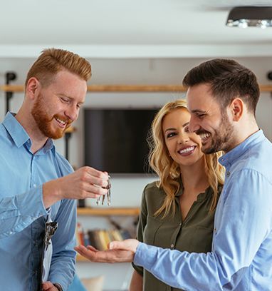 Real estate agent handing keys to a smiling couple in a home.