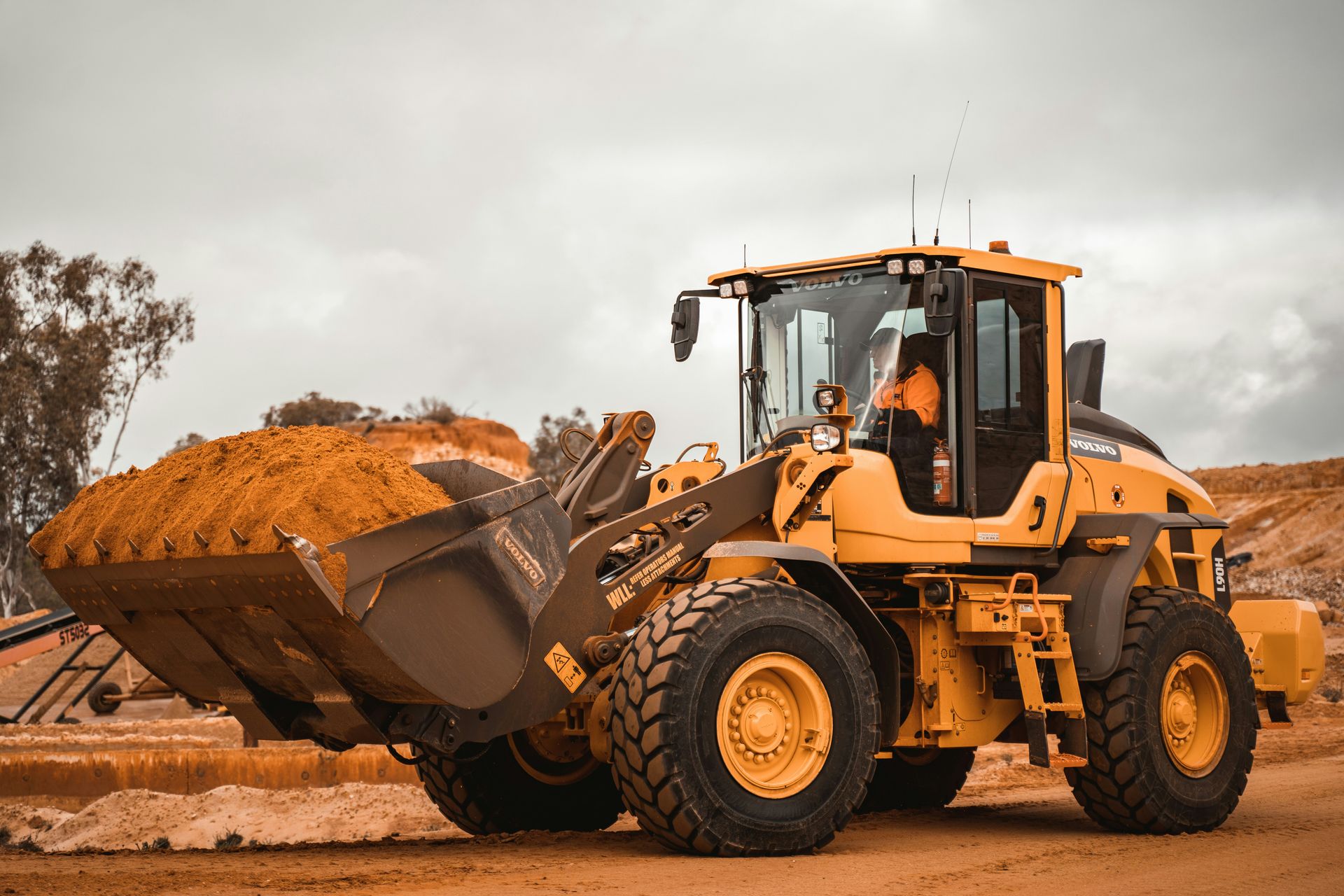 Front end loader carrying a bucket of dirt on a civil construction site.