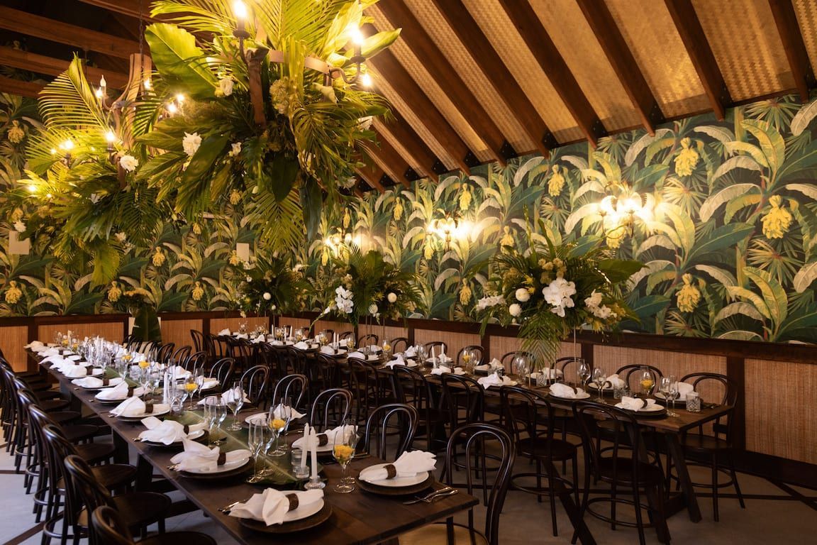 A long table with plates , glasses , and candles in a room with a chandelier hanging from the ceiling.