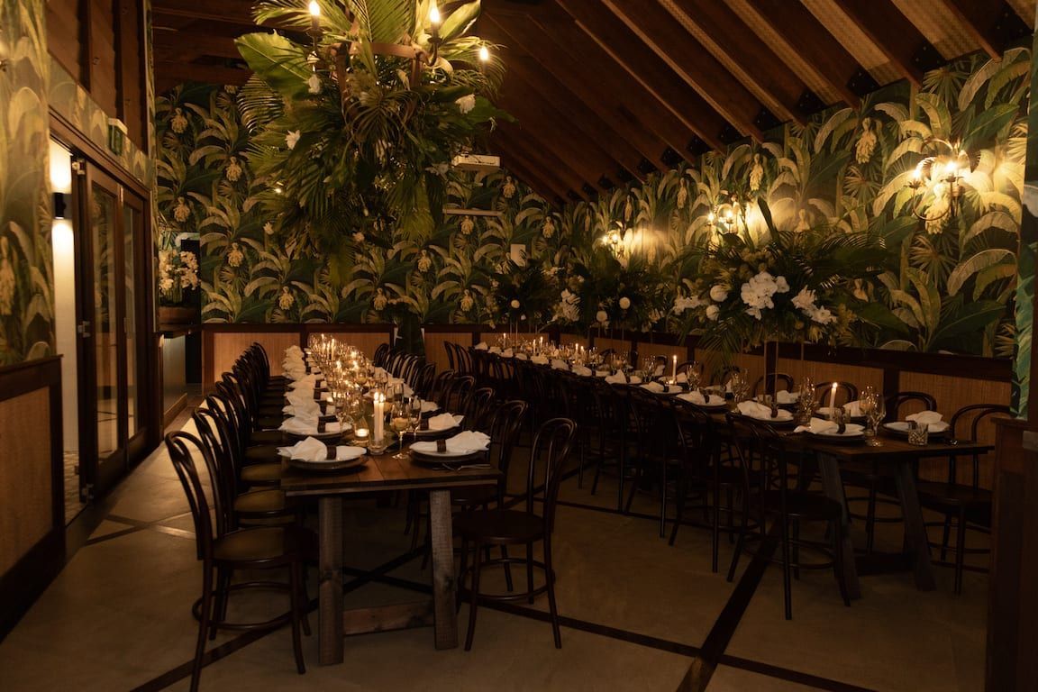 A dining room with a long table and chairs and a chandelier hanging from the ceiling.