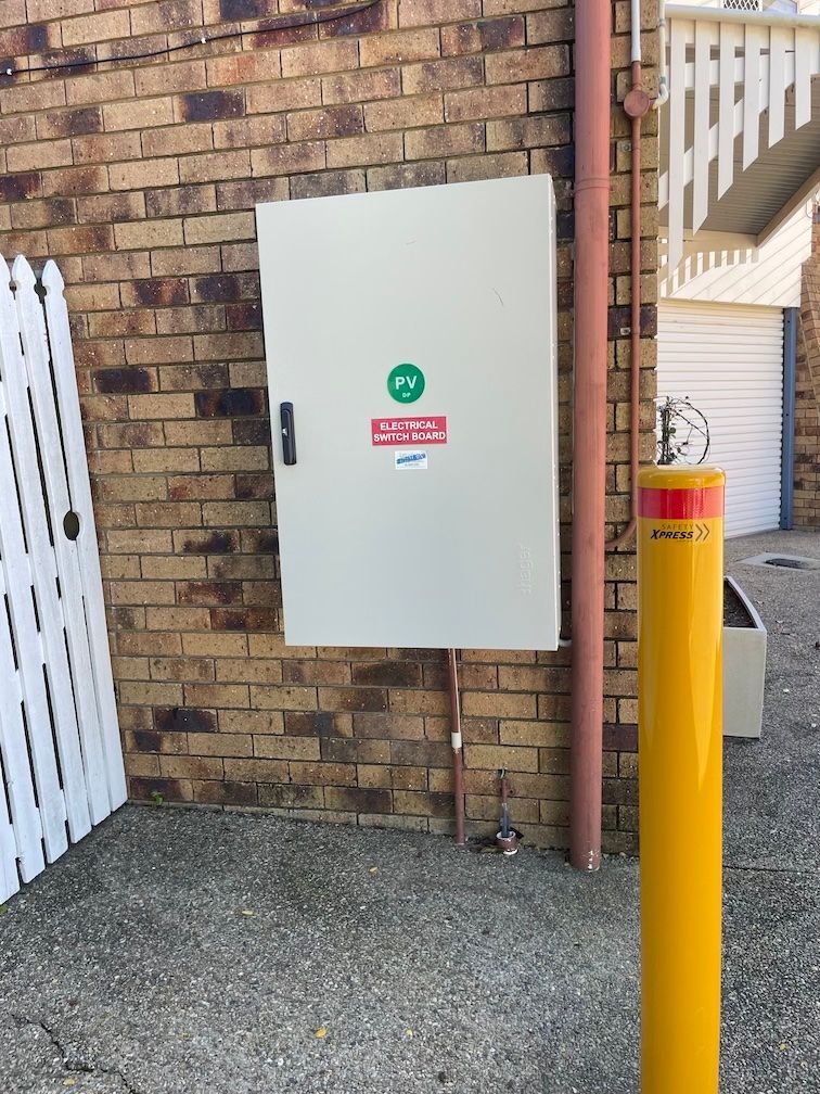A yellow pole is next to a white box on a brick wall