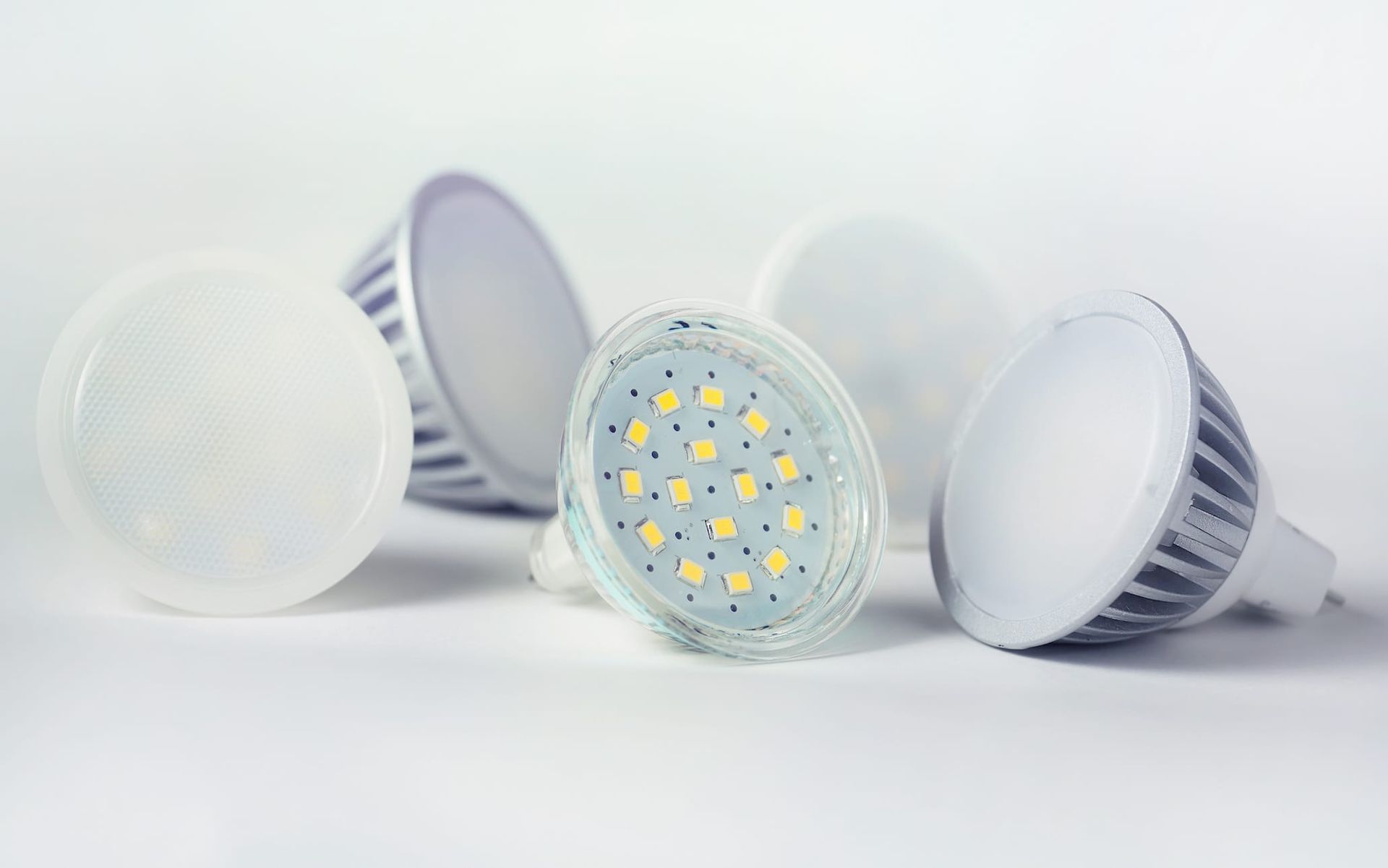 Close-up of several LED light bulbs on a white surface; some are round and opaque, others have exposed LEDs.