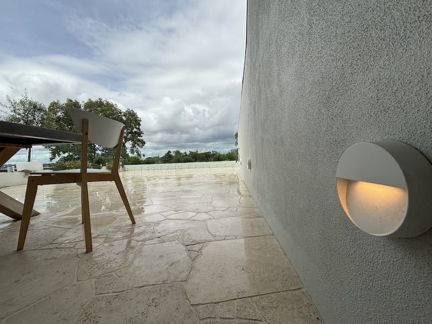 A table and chairs are sitting on a patio next to a wall with a light on it.