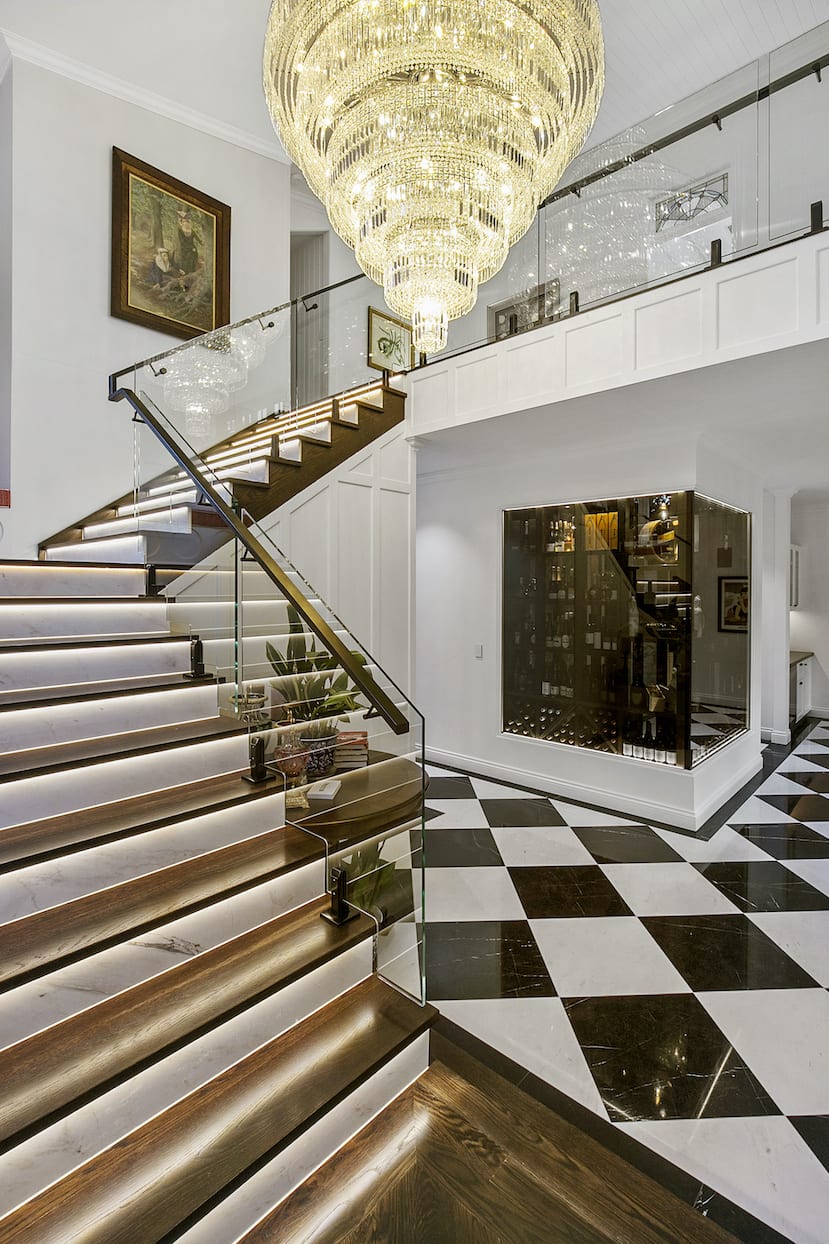 A staircase in a house with a checkered floor and a chandelier hanging from the ceiling.