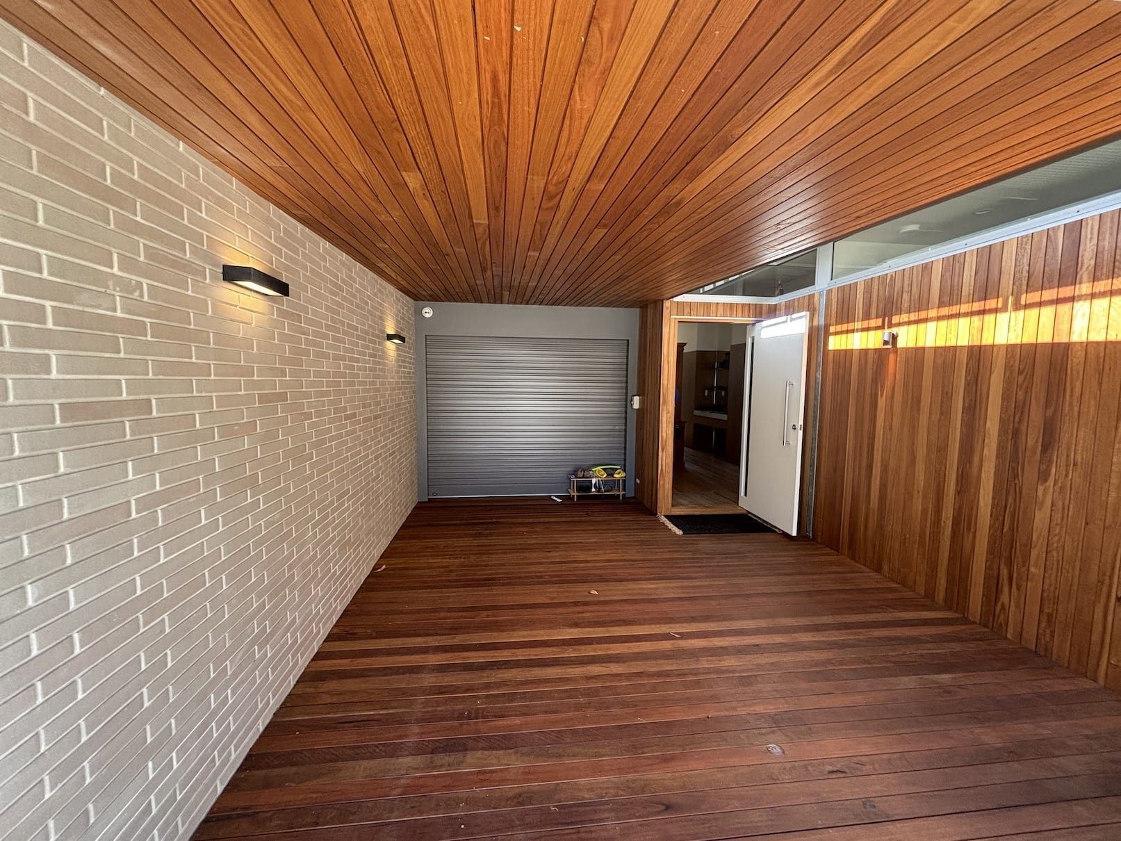 A long hallway with a wooden floor and a wooden ceiling leading to a garage.