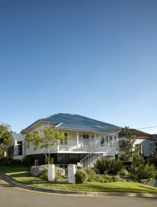 A large white house with a blue roof is sitting on top of a lush green hillside.