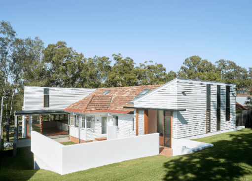 A white house with a red roof is surrounded by trees and grass.
