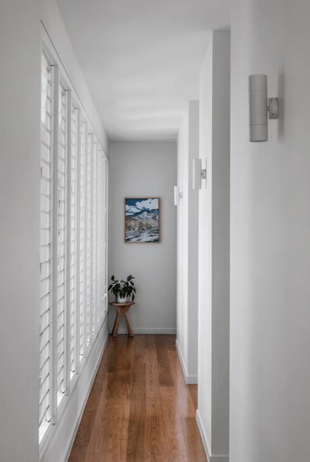 A long hallway with shutters on the windows and a painting on the wall.