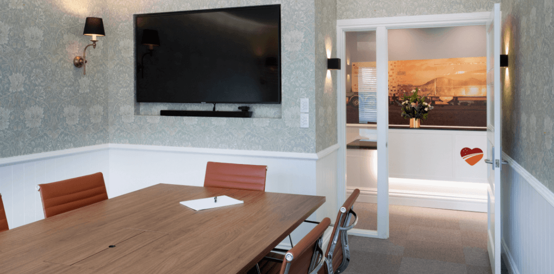 A conference room with a table and chairs and a flat screen tv on the wall.