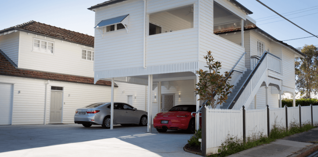 A red car is parked in front of a white house.