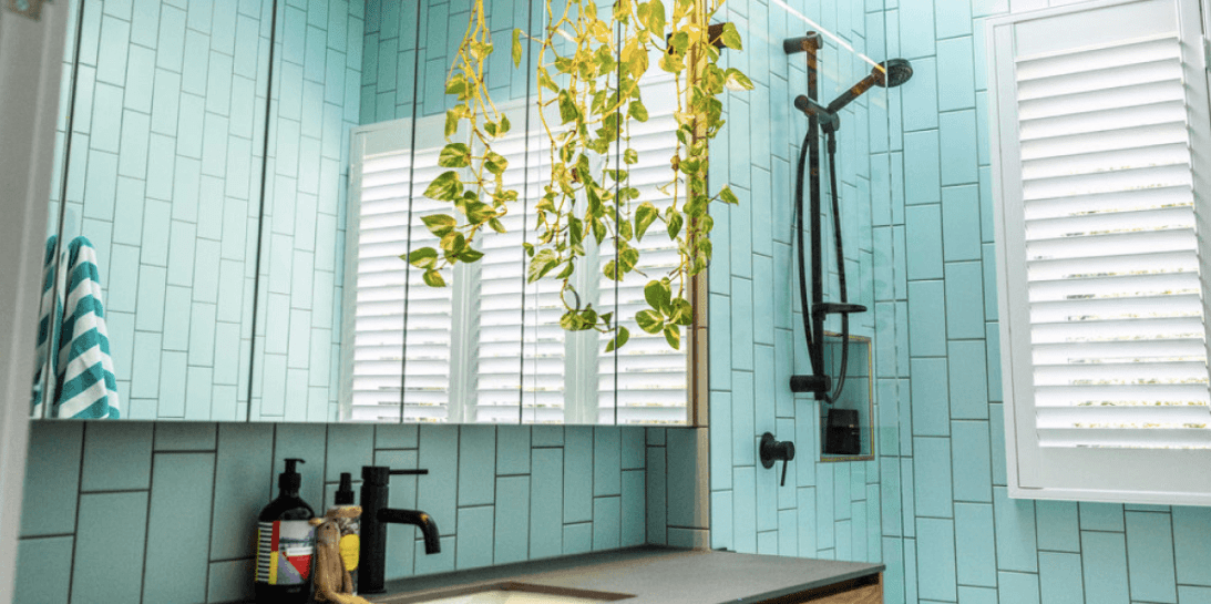 A bathroom with blue tiles , a sink , a mirror and a shower head.