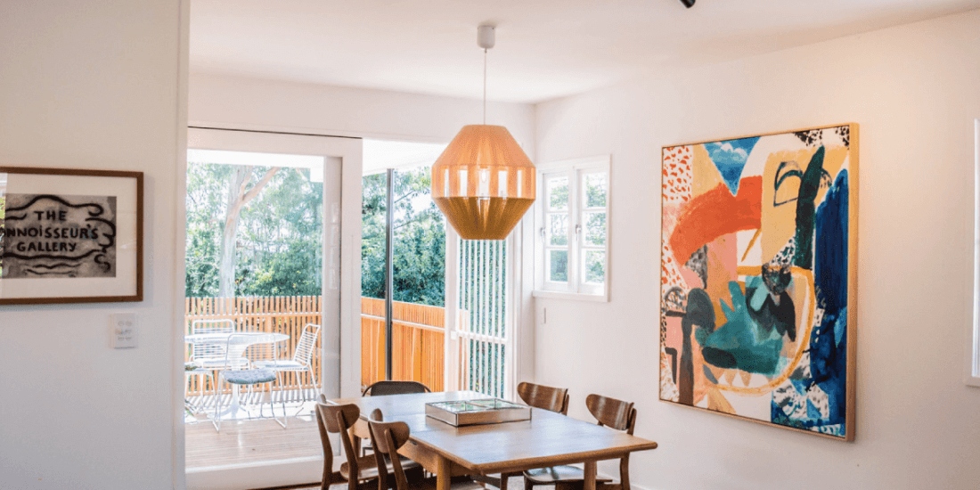 A dining room with a table and chairs and a painting on the wall.