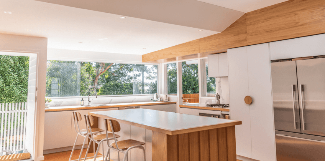 A kitchen with white cabinets , stainless steel appliances , a large island , and a large window.