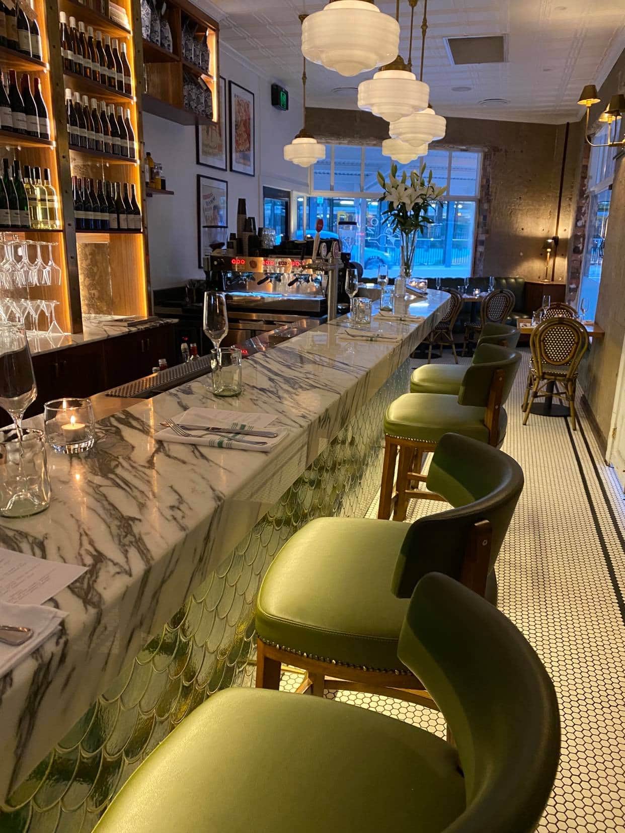 A long marble bar with green chairs in a restaurant.