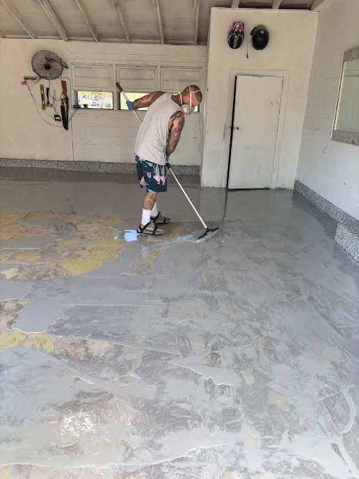 Person applying coating to a garage floor with a squeegee. Floor is partially coated.