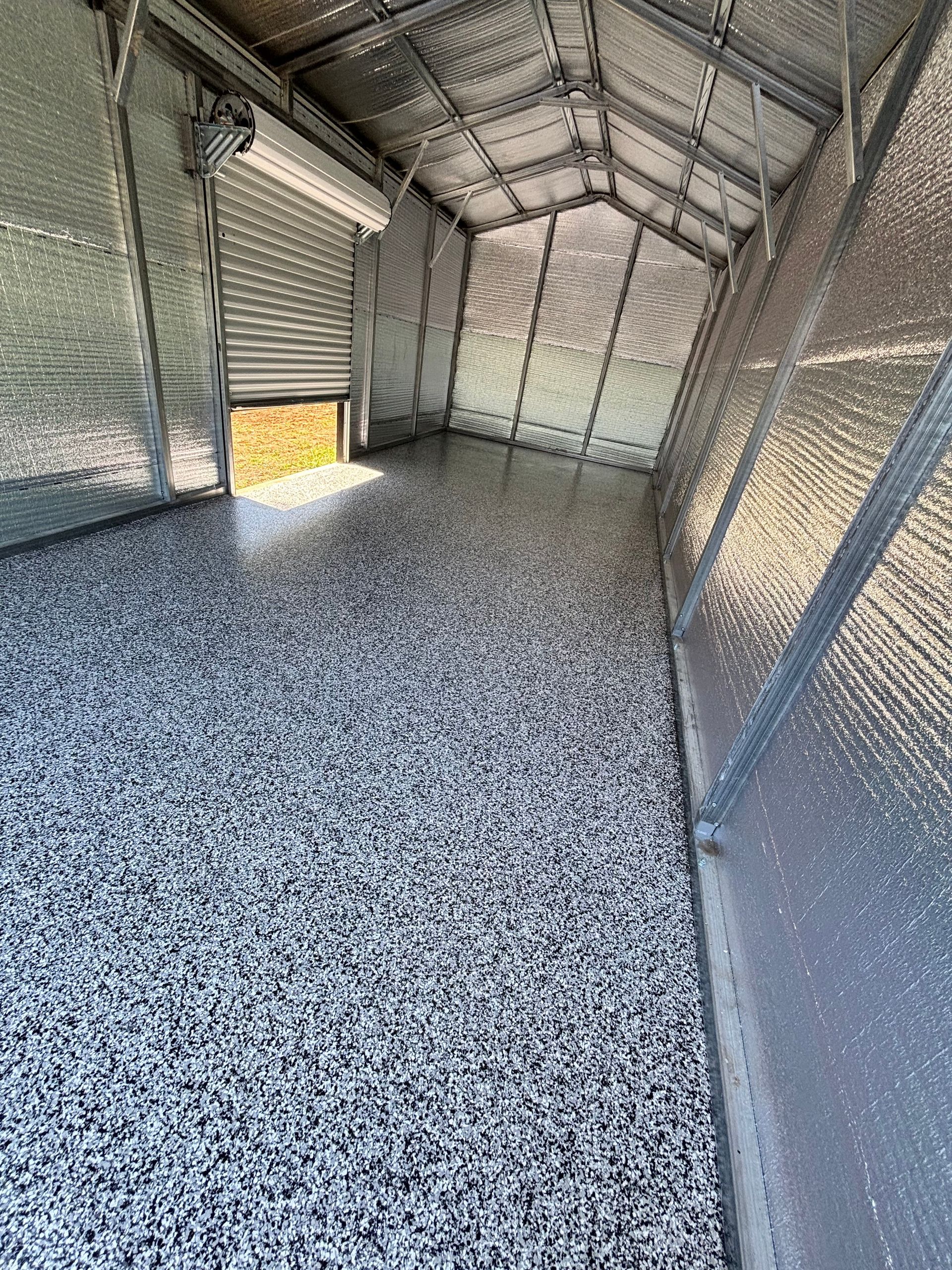 Inside a shed with a speckled epoxy floor and insulated walls; the roll-up door is partially open.
