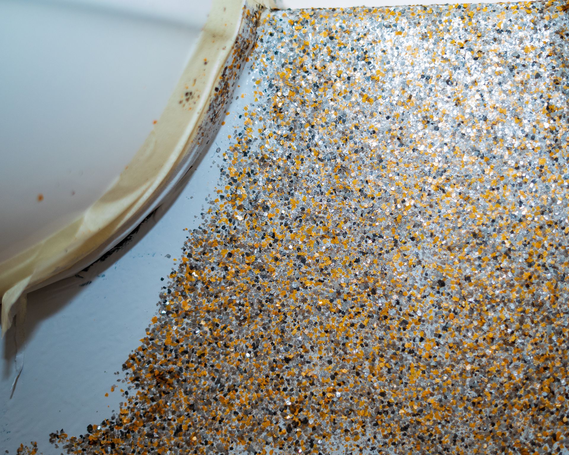 Scattered glitter in shades of silver, gold, and brown near a white surface and adhesive tape.