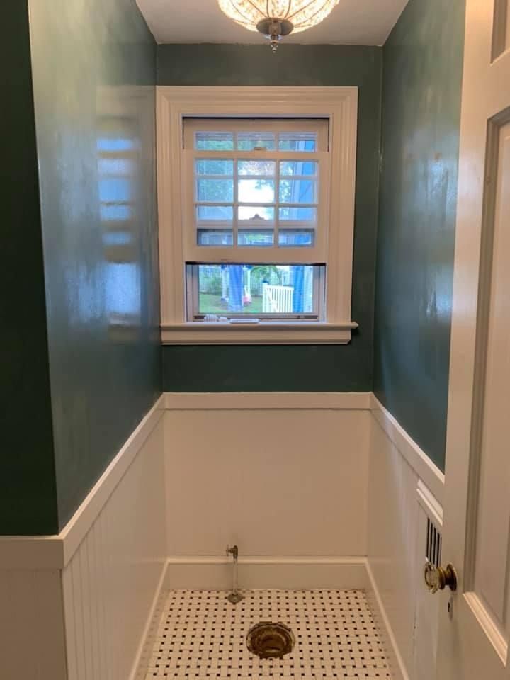 Small shower stall with green walls, white wainscoting, and a window above the built-in shelf.