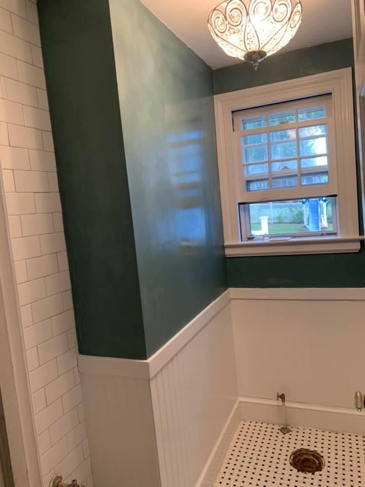 Small bathroom with white wainscoting, green walls, window, and tiled shower floor with drain.