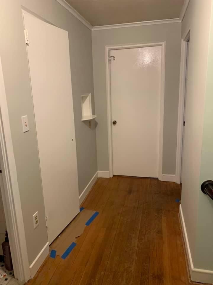 Narrow hallway with gray walls, white doors, wood floor, and blue tape on the floor near the left wall