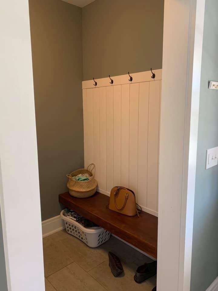 Small entryway nook with hooks, a wooden bench, baskets, shoes, and a built-in white panel wall.