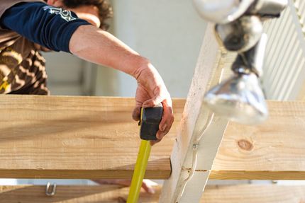 Person measuring wooden boards with a tape measure near a sink outdoors