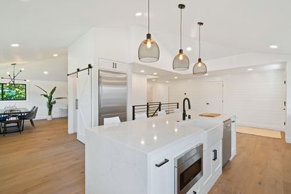 Bright modern open kitchen with white island, pendant lights, wood floors, and adjacent dining area