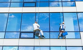 Two window washers, suspended by ropes, cleaning windows on a tall building.