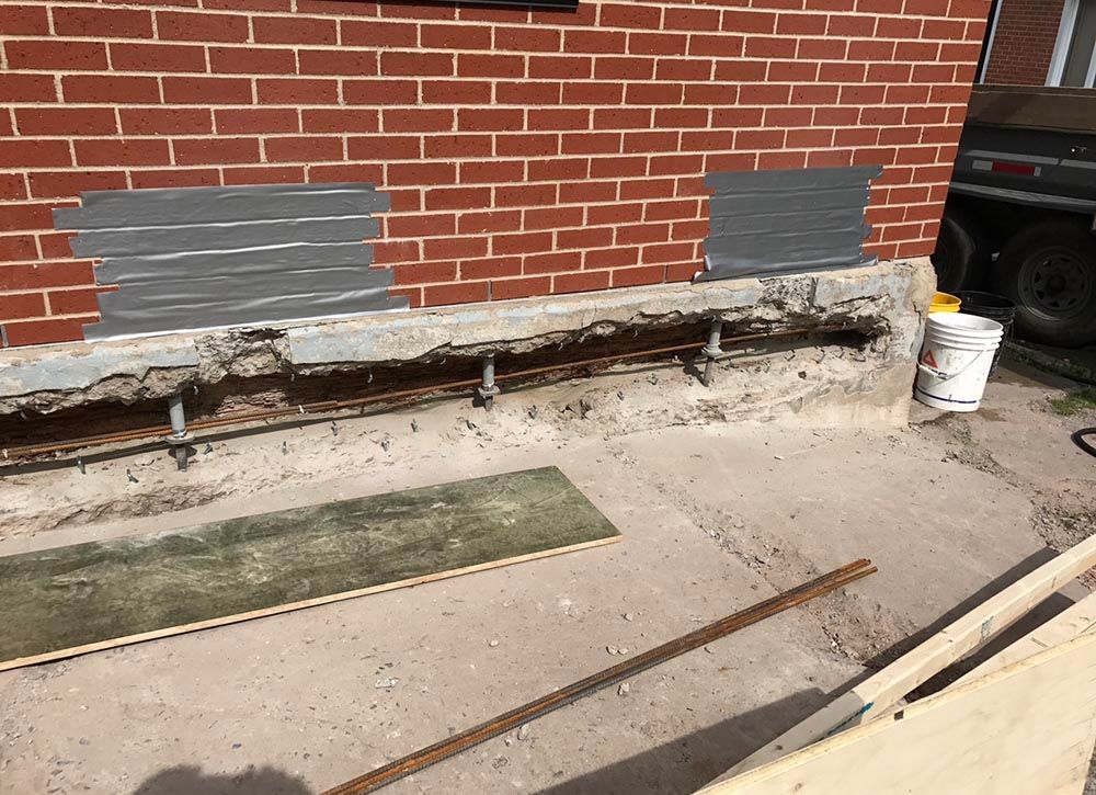 Un mur de briques est en train d'être réparé avec du ruban adhésif et du béton.