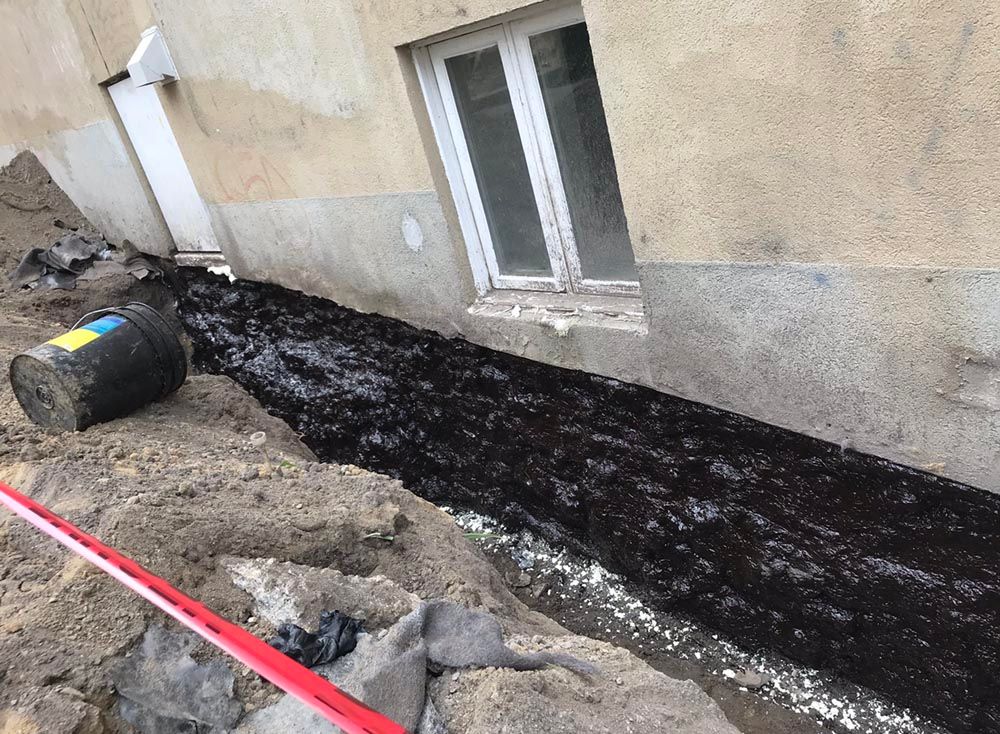 Un grand tonneau noir est posé sur le côté d'un bâtiment à côté d'une fenêtre.