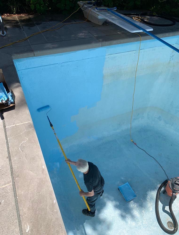 Un homme peint une piscine avec un rouleau.