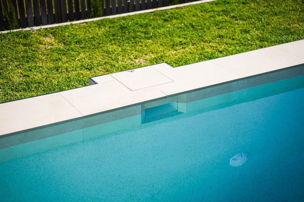 A Light Blue Swimming Pool With a Gray Edge Next to Green Grass — Concrete Pool Projects in Gladstone Central, QLD