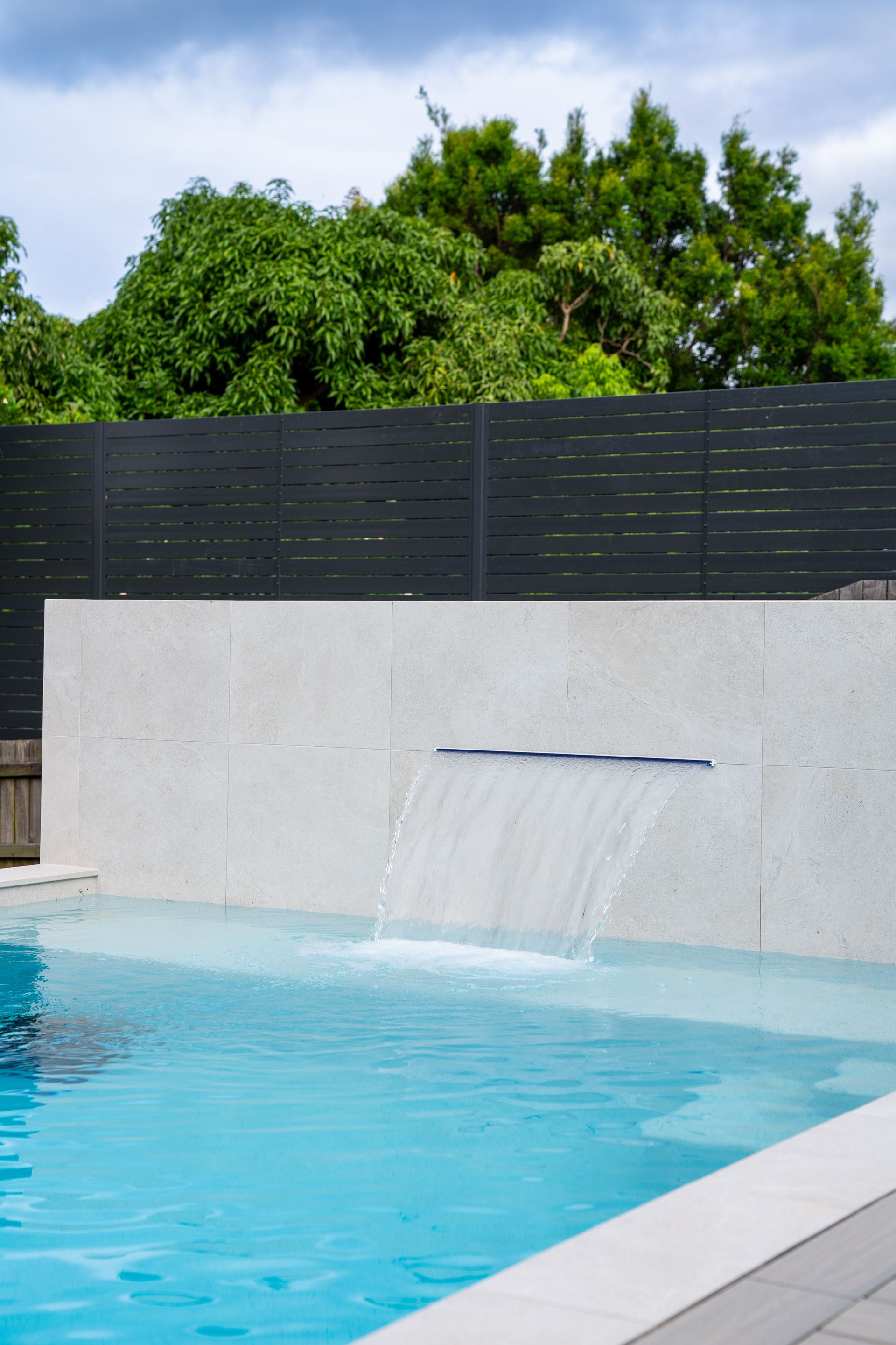 Swimming Pool With Blue Water, Tan Border, and a Metal Ladder — Concrete Pool Projects in Calliope, QLD