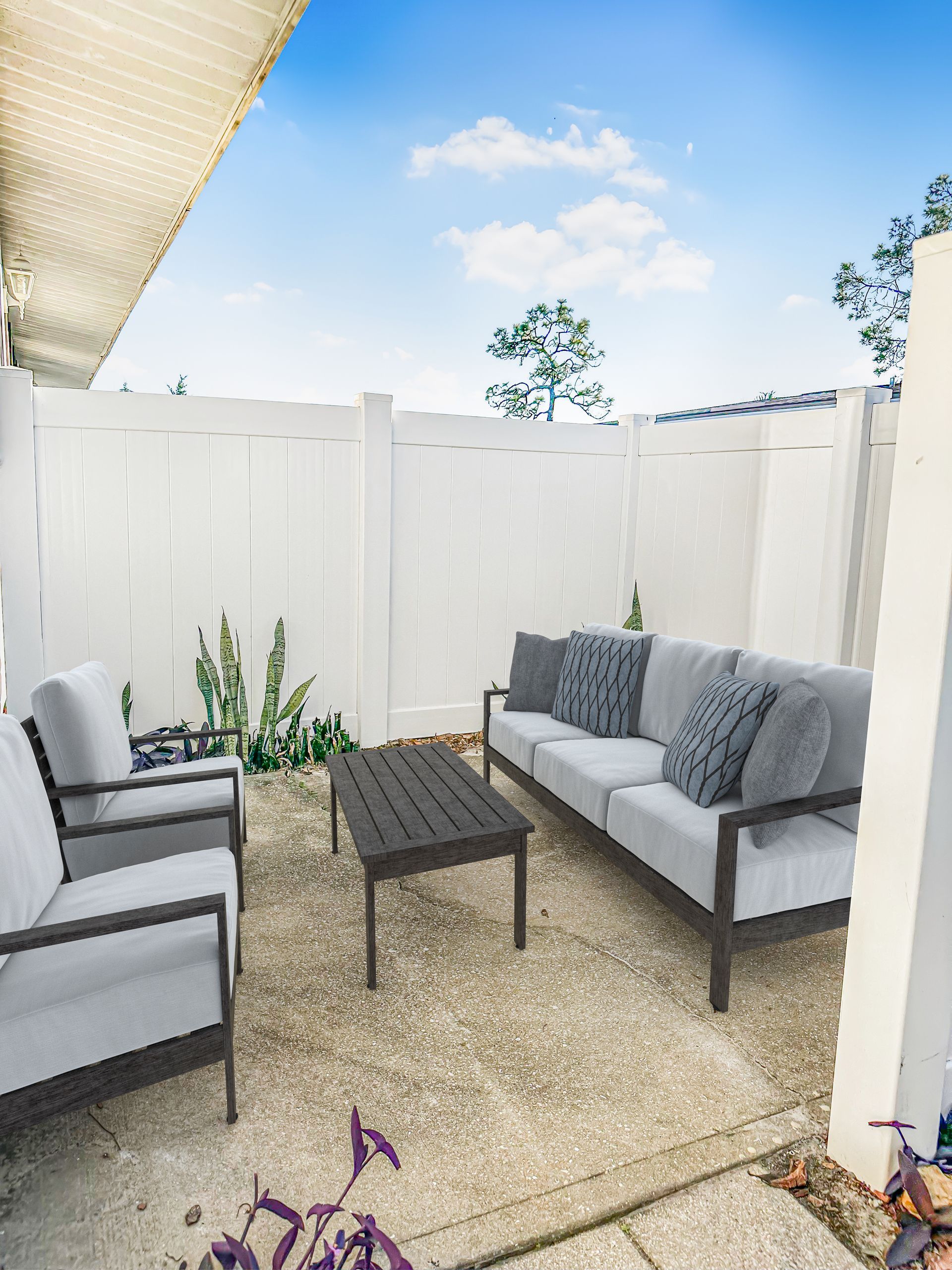 Photo of a patio, showing a cozy space for gathering or relaxing, surrounded by a tall, white privacy fence