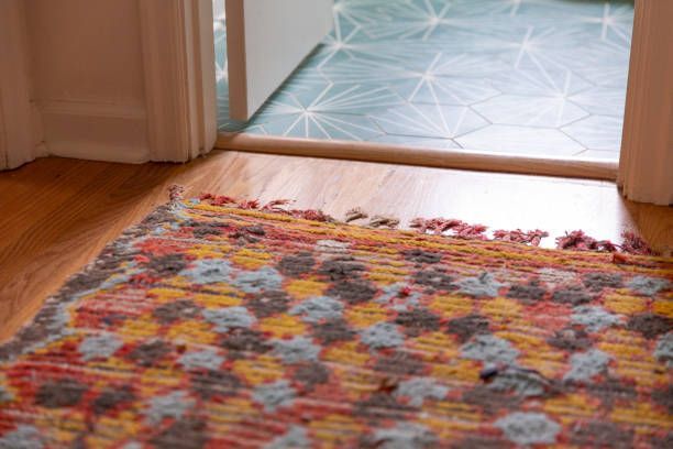 A dachshund peeking out from under a couch on a carpet.