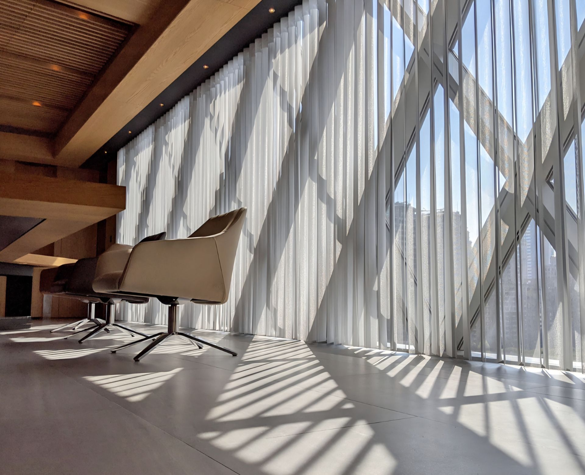 Modern office interior with sheer curtains, chair shadows on floor.